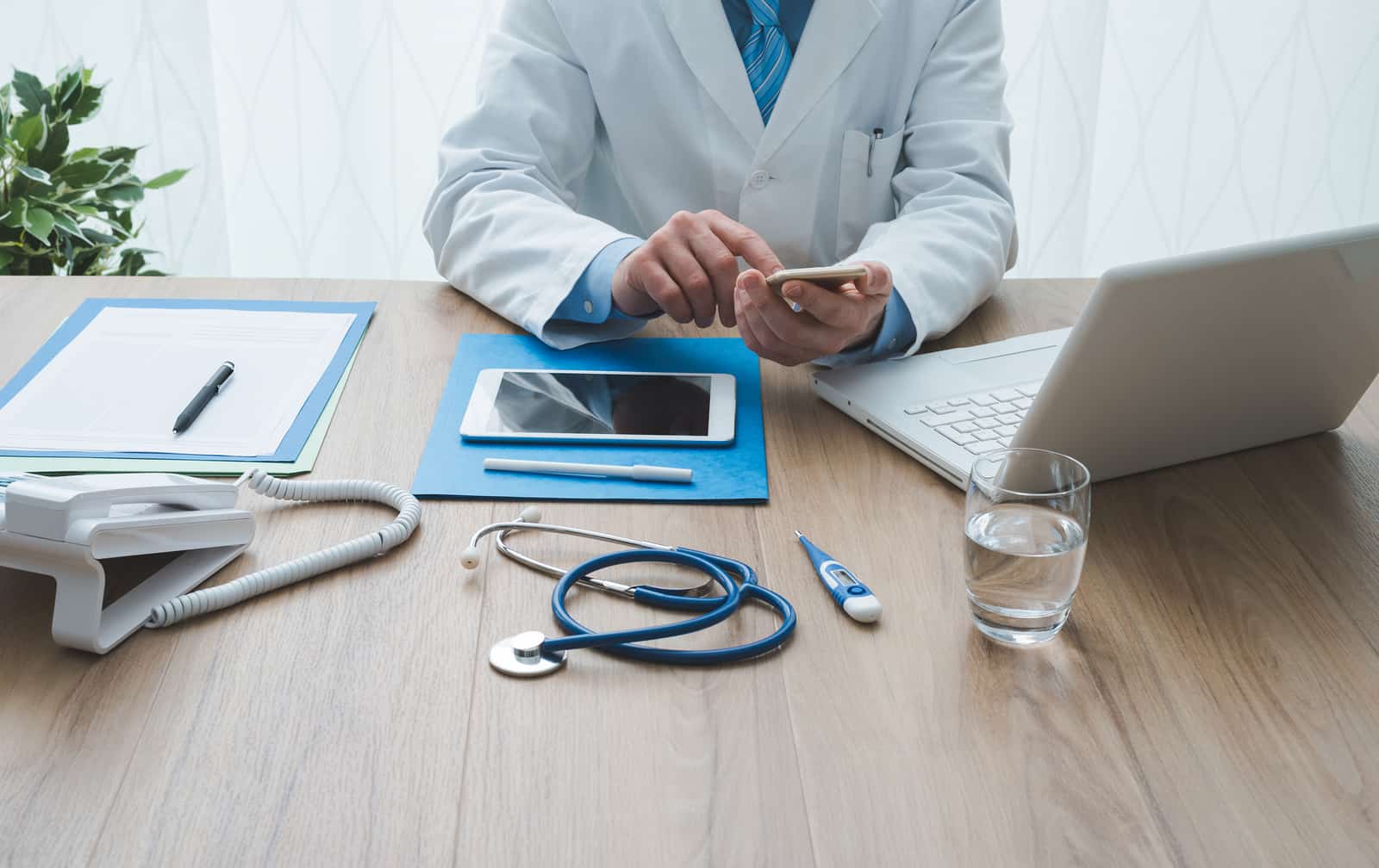 A doctor working at their desk using a laptop, tablet, and smartphone